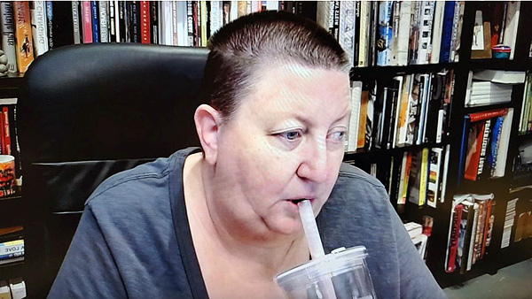A photograph of a woman sipping from a straw in a cup and books on shelves in background
