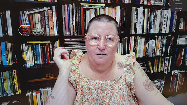 A photograph of a woman wearing glasses and a flowery dress and books on shelves in background