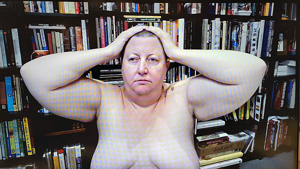 A photograph of a woman not wearing a shirt with her hands on either side of the top of her head looking to the right of the camera and books on shelves in background