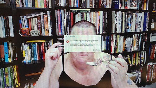 A photograph of a woman holding a spoon in her left hand with a computer message that popped up in front of her face and books on shelves in background