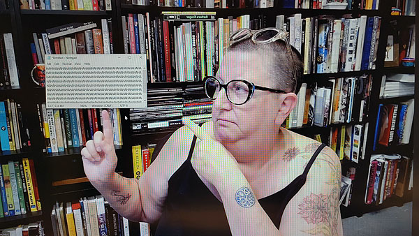 A photograph of a woman wearing a pair of glasses on her face over her eyes with another pair on top of her head, both forefingers pointing to a rectangle with a repeating pattern of HA HA and books on shelves in background