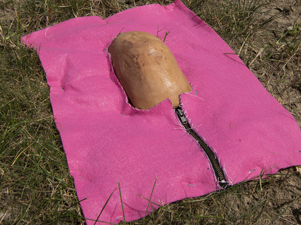 This is a picture of a fake elbow poking through a hole in a pink life jacket in grass by Richard Haley