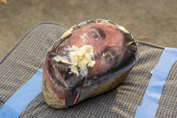 This is a picture of a mankin head with margarine in it's mouth on a cousion by Richard Haley